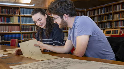 Two students sitting in the library looking at a music manuscript