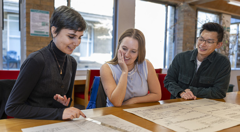 three students sitting in the library looking at music manuscripts