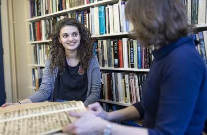 A student and teacher pictured discussing a manuscript  in front of a bookcase